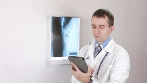 The doctor checks the patient data on the tablet. White wall and the X-ray Video stock 73633342