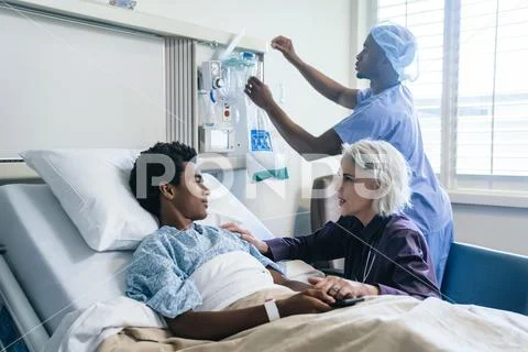 Doctor comforting boy laying in hospital bed Stock Photos