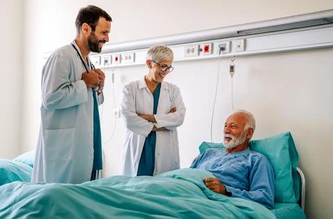 Doctor consulting happy senior man patient on hospital bed. Healthcare and Stock Photos