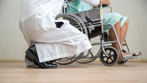 Doctor Crouching By Disabled Man Over Wheelchair On Floor Stock Photos