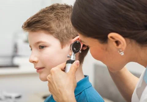 Doctor examining boy ear , using otoscope, in doctors office. Child receiving Photos