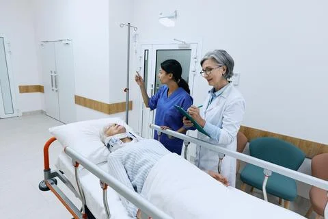 Doctor examining elderly patient with neck injury lying on medical gurney wit Stock Photos