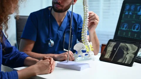 Doctor explains spinal anatomy with model and X-ray to patient during consu.. Video stock 312383524