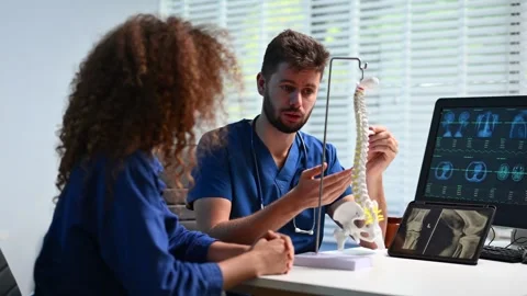 Doctor explains spinal anatomy with model and X-ray to patient during consu.. Vídeo Stock 312386747