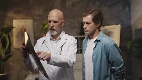 Doctor explains X-ray results to male patient during medical consultation Stock Footage 342749760