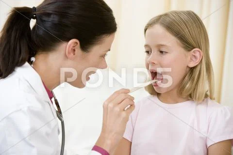 Doctor giving checkup to young girl with tongue depressor in exam room Stock Photos