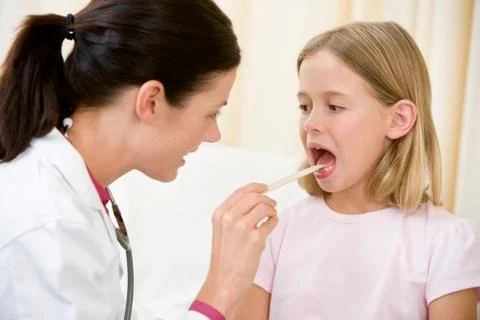 Doctor giving checkup to young girl with tongue depressor in exam room Stock Photos