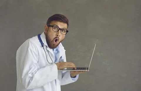 Doctor in glasses using laptop computer and looking away with funny surprised Stock Photos