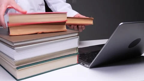 Doctor hands adding old academic books to a stack beside a modern laptop Stock Footage 324762829