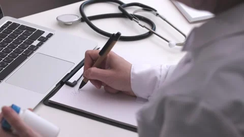 Doctor hands working white table writing on clipboard using pen hold drug bottle Stock Footage 246645094