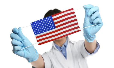 Doctor holding medical mask with USA flag pattern on white background. Danger Stock Photos