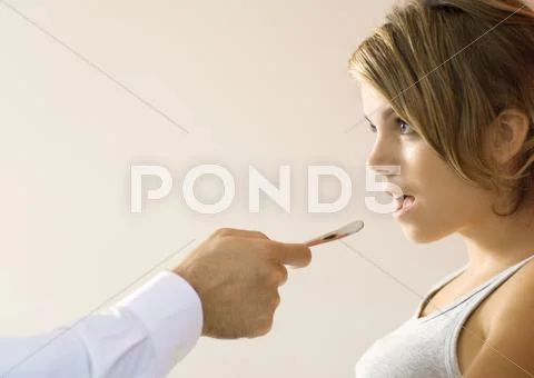 Doctor Holding Out Tongue Depressor Toward Young Woman's Mouth