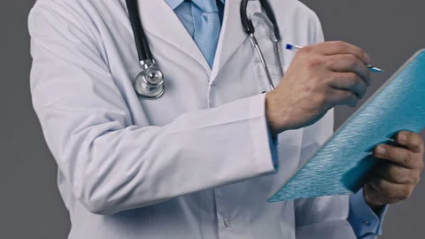 Doctor holds a tablet folder in hands and writes data with a ballpoint pen Stock Footage 130756488