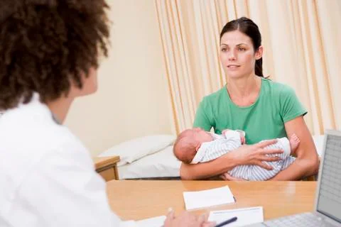 Doctor with laptop and woman in doctor's office holding baby Stock Photos