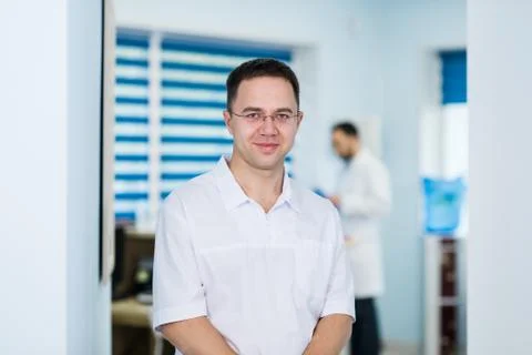 Doctor looking at camera while his colleague discussing in medical office Stock Photos