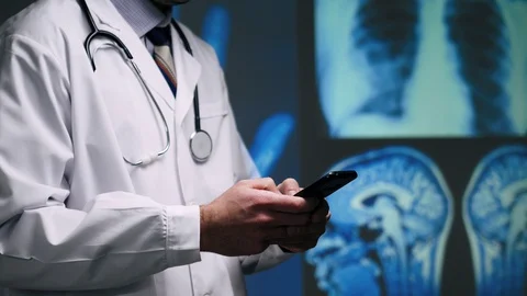 Doctor Looking at a X-Ray Scan and MRI Brain Imaging on a Smartphone Device Stock Footage 127128523