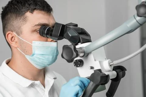 A doctor looks through a microscope in close-up. Dental microscope at work. The Stock Photos