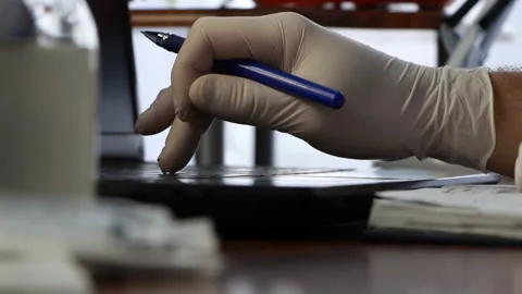 The doctor makes notes on the computer with a pen in one hand and white gloves Stock Footage 86953506