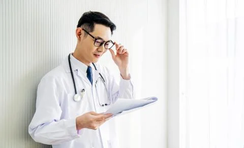 Doctor man looking down reading to his patient notes standing in hospital Stock Photos