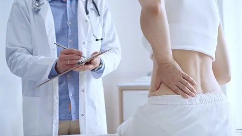 Doctor man is making notes on a clipboard while patient woman is 스톡 사진