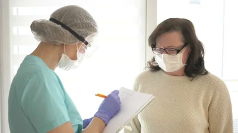 Doctor in a medical mask, goggles and disposable gloves records the results of a Stock Footage