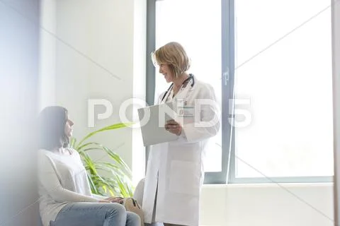 Doctor With Medical Record Talking To Patient In Waiting Room