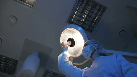 The doctor in the operating room directs light on the patient and is preparing Stock Footage