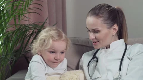 Doctor pediatrician talking while sitting on a sofa with a cute blond child. Stock Footage 135350786