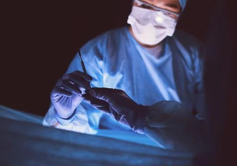 Doctor performing surgery in a dark background. Stock Photos