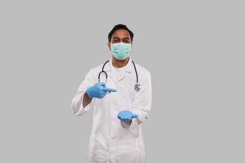 Doctor Pointing at Empty Open Hand in front of Chest Wearing Medical Mask and Stock Photos