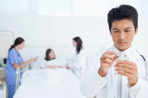 Doctor preparing a syringe while his colleagues are treating a patient 스톡 사진