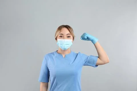 Doctor with protective mask showing muscles on light grey background. Strong  Stock Photos
