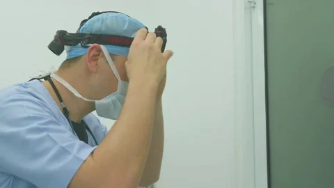 Doctor replacing the head gear light with the surgical loupes in operating room Stock Footage 77449414