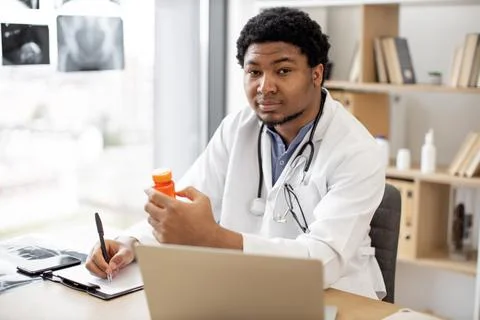 Doctor reporting about pills using laptop in clinic's office Stock Photos