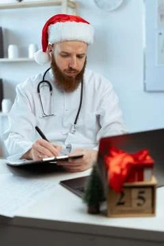 Doctor in santa hat working on the shift on Christmas eve in the hospital Фото