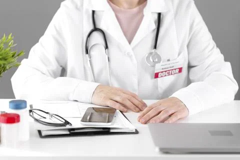The doctor sits at a white table with papers and jars for analysis. Stock Photos