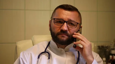 Doctor sitting in the office and looks angry while speaking on cellphone Stock Footage