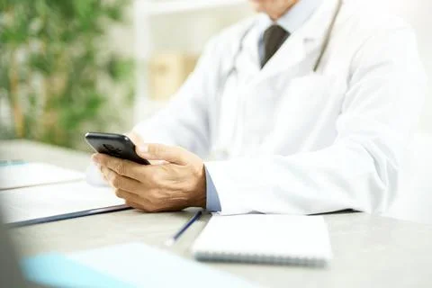 Doctor sitting at the table and using modern smartphone Stock Photos