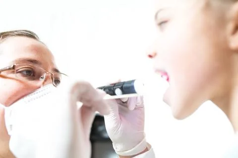 A doctor with a spatula and a flashlight checks the throat of a sick child Stock Photos