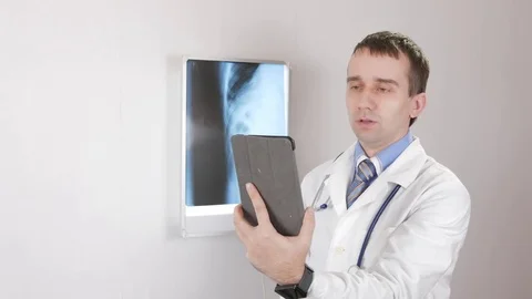 The doctor speaks with pachinte on the Internet using a tablet. White wall and Stock Footage 73633840