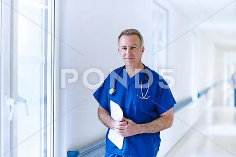 Doctor Standing In Corridor Holding Medical Records
