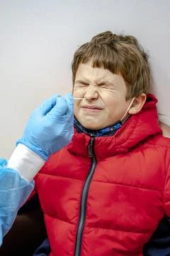 Doctor tacking a coronavirus test to an elementary age boy's nose with a medi Stock Photos