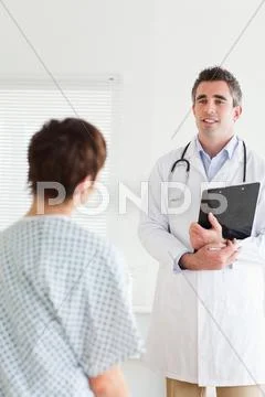 Doctor talking to a cute woman in hospital gown Stock Photos