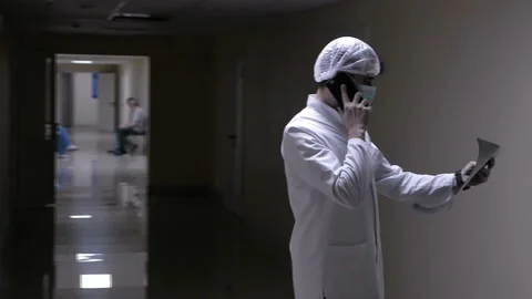 Doctor talking on the phone with a patient holding an x-ray in his hands walking Stock Footage