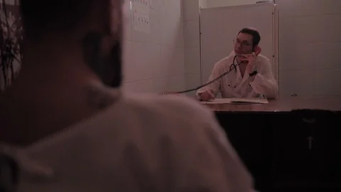 Doctor is talking on the phone while the maniac and the killer tied to a chair Stock Footage 126001435