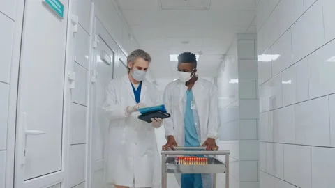 Doctor talks with nurse while walking at the hospital hall, carrying test tubes Video stock 166665123
