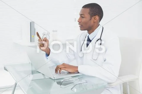 Doctor text messaging while using laptop at medical office Stock Photos