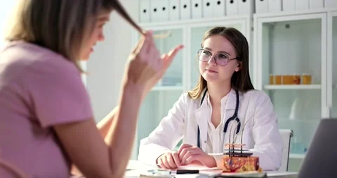 Doctor trichologist discusses problem of split ends with woman in clinic Stock Footage 233200493