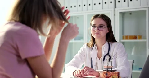 Doctor trichologist looks at split ends of female patient in clinic Stock Footage 232619837