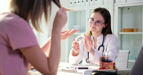 Doctor trichologist offers cure for split ends to female patient in clinic Stock Footage 234599625